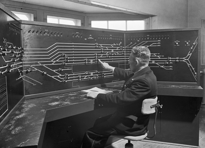 159670 Interieur van het seinhuis van de N.S. te 's-Hertogenbosch met de treindienstleider achter het NX-bedieningstableau.